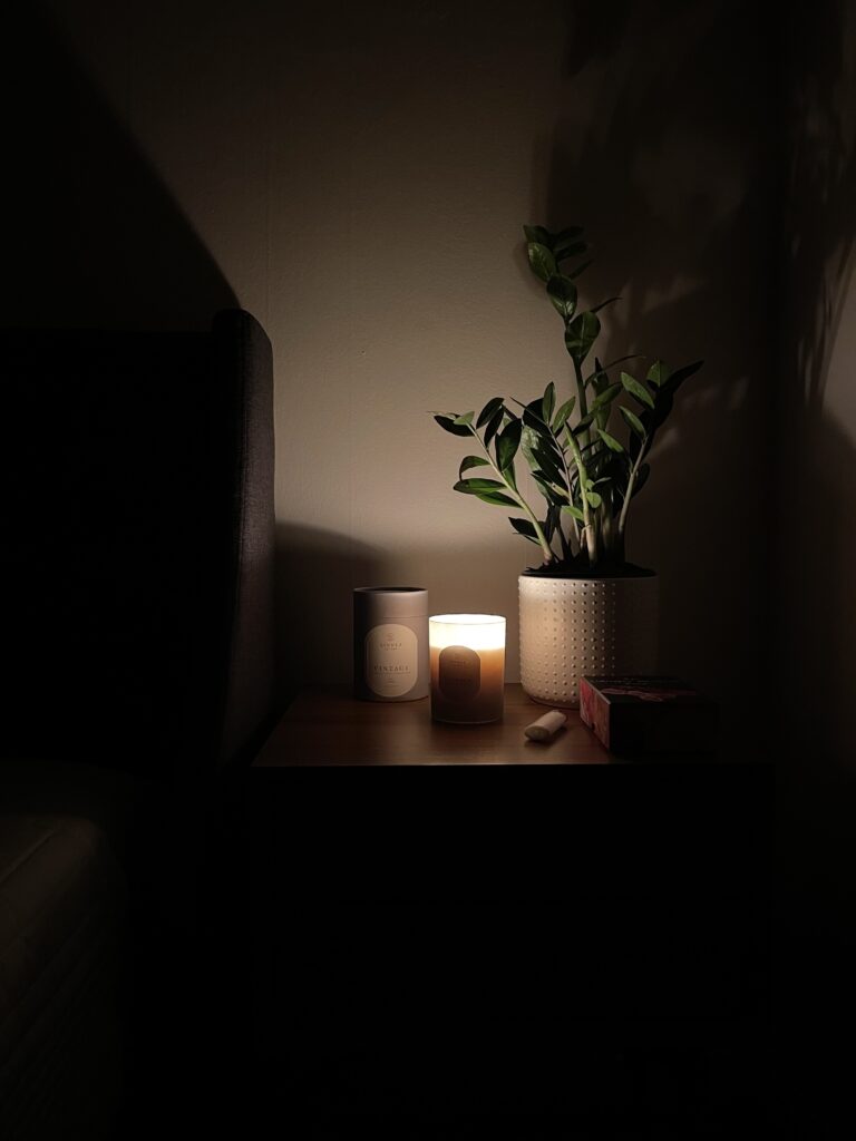 A candle on a nightstand burns in a dark bedroom. 