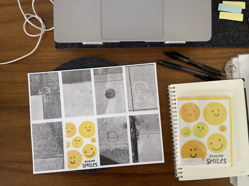 A sheet of paper with images of sidewalk smiley faces that hasn't yet been folded into a zine and a smiley face greeting card atop my desk. 