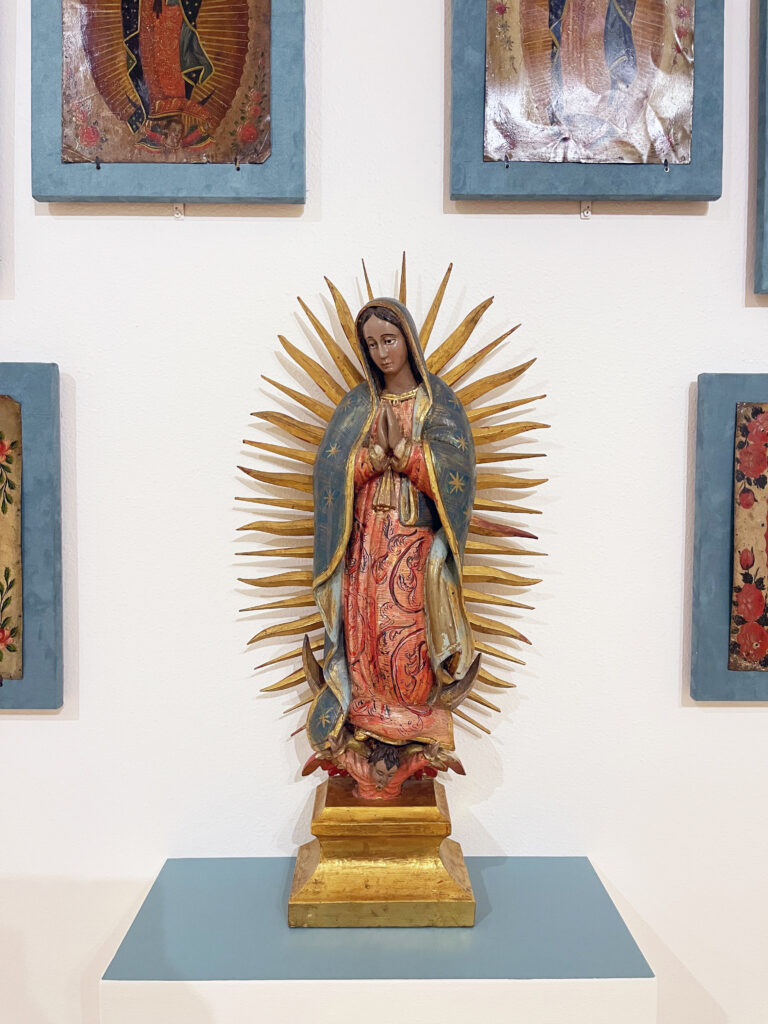 A small figure of the Virgin of Guadalupe surrounded by small framed images of the same Virgin, on display at the El Paso Museum of Art, May 2022. 