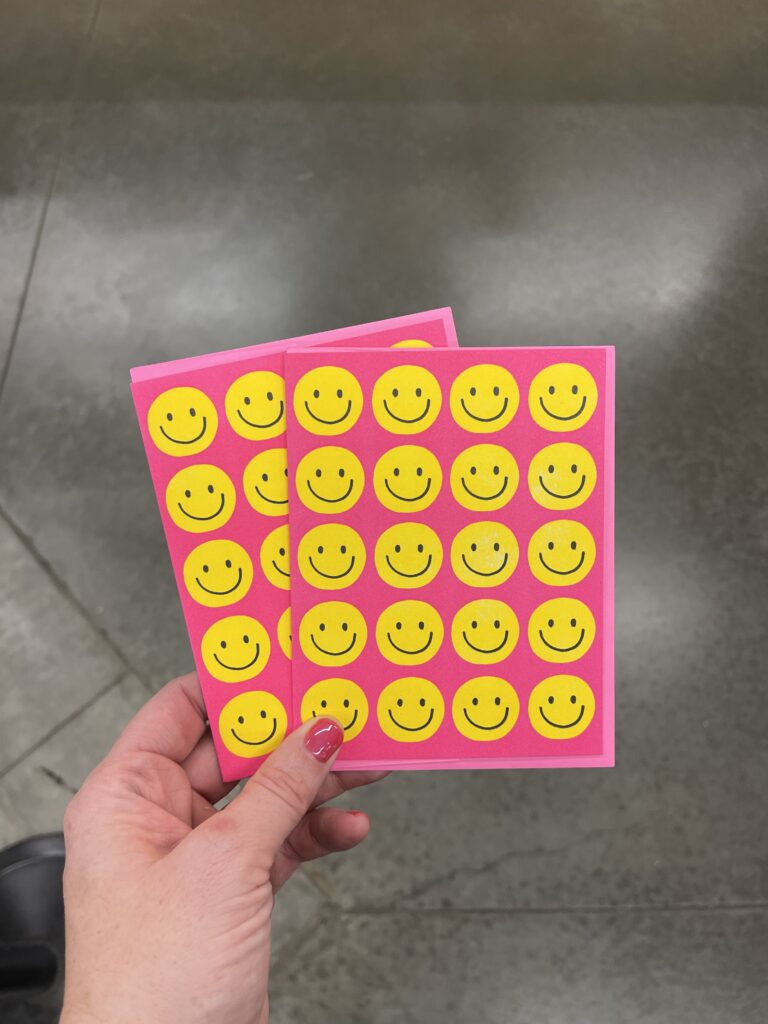 Two hot pink greeting cards with 5 rows of 4 yellow smiley faces each covering the front of the card. 