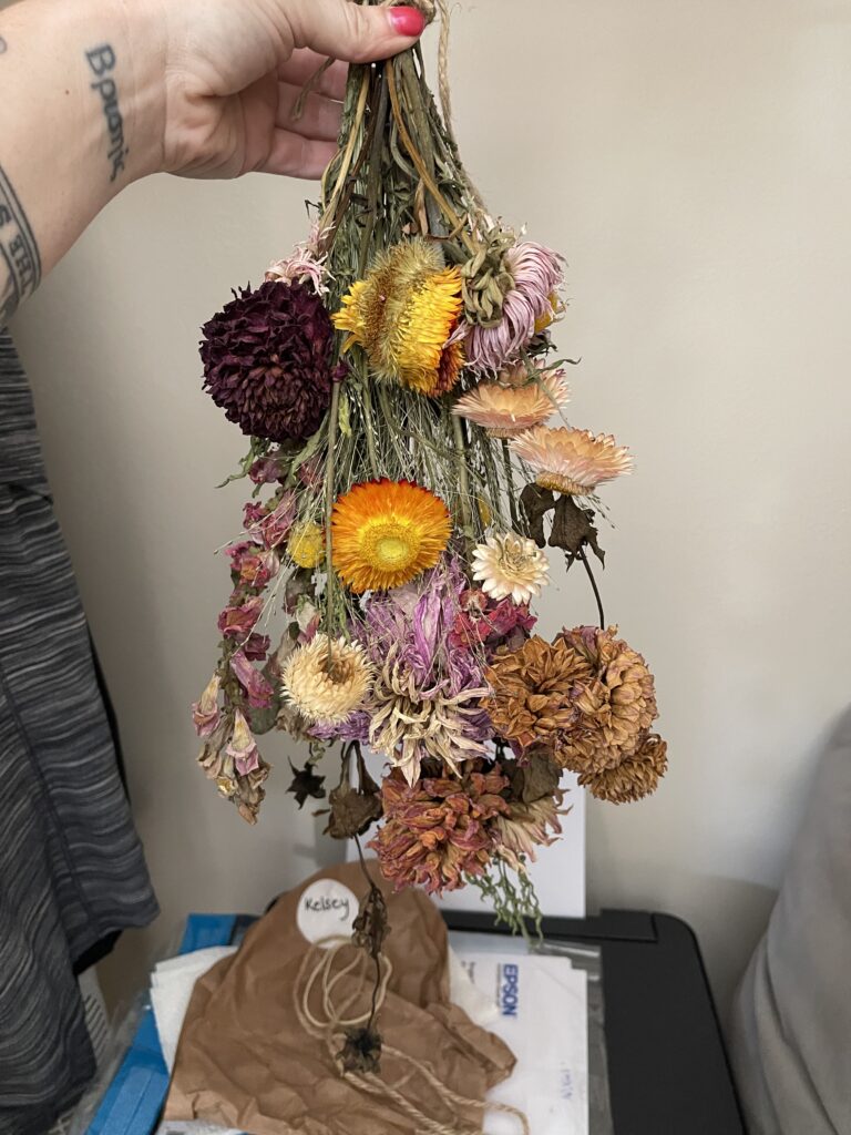 A dried bouquet of flowers being held upside down by yours truly. The reds, pinks, oranges, and yellows of the flowers have retained their color pretty well after weeks of drying in a dark coat closet. 