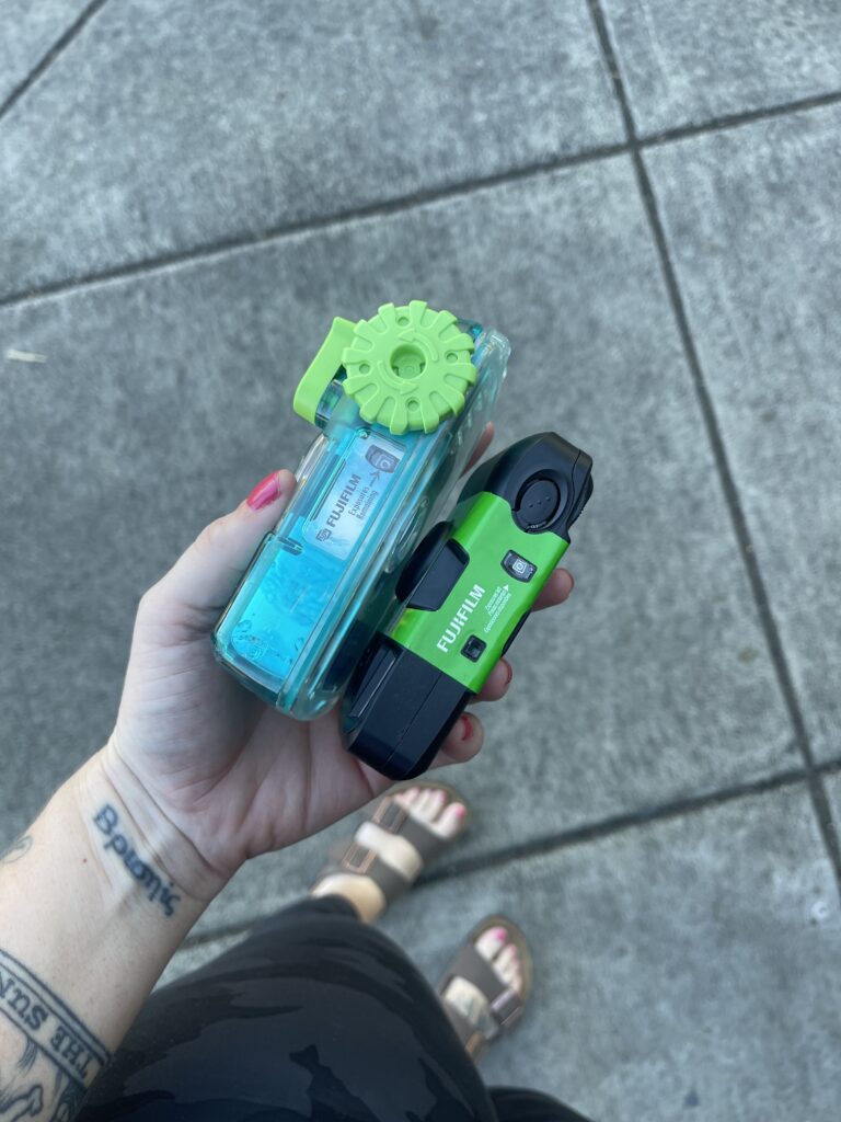 Holding two disposable cameras in my hand outside a local shop that still develops film on-site. 